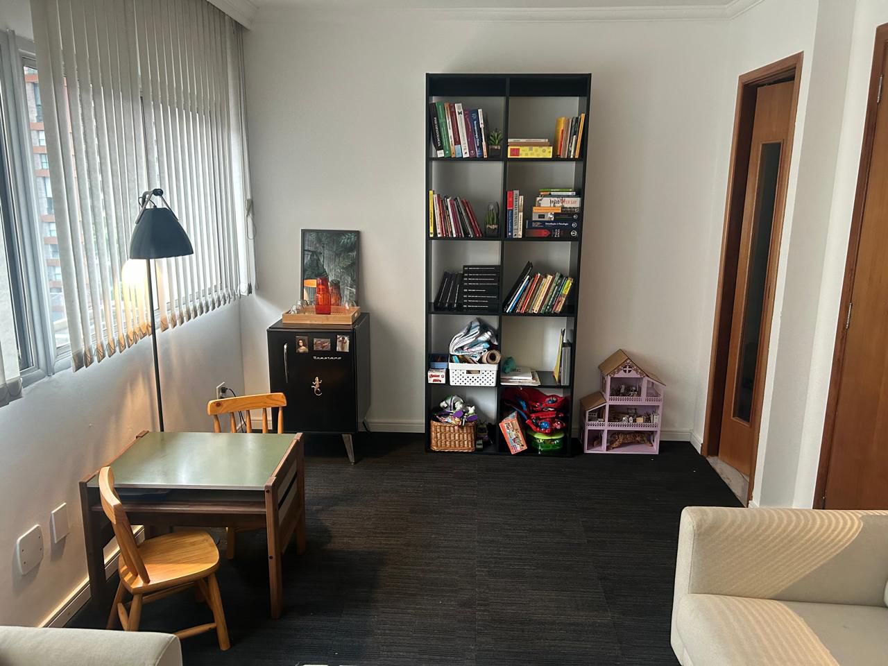 Sala de atendimento de Júlia Zimmermann no Itaim-Bibi, com estante de livros e uma mesa.